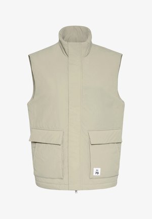 Ljusbeige ärmlös vadderad väst med hög krage, framslte dragkedja täckt av klaff, två stora fickor med klaffar och liten "M 73"-etikett.