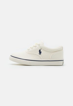 Baskets basses en toile blanc cassé avec lacets à l'avant, logo bleu marine représentant un joueur de polo sur le côté, et fine bande bleu marine sur la semelle blanche.
