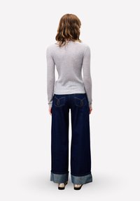 Pull gris côtelé associé à un jean large bleu foncé avec des coutures contrastantes et des revers roulés ; personne vue de dos.