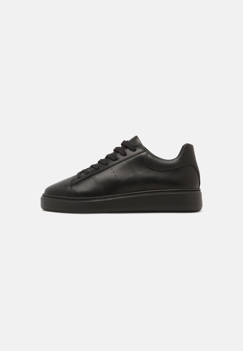 Baskets basses noires avec lacets à l'avant, tige en cuir lisse et semelle épaisse, présentées en profil latéral sur un fond uni.