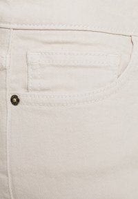 Witte denimspijkerbroek met een voorzak, subtiele textuur, contrasterende stiksels en een metallic accent op de zak.