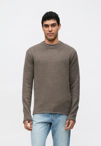 Ruskea teksturoitu neulepaita pyöreällä pääntiellä ja pitkillä hihoilla, yhdistetty vaaleansinisiin farkkuihin. Kangas näyttää pehmeältä ja miellyttävältä.