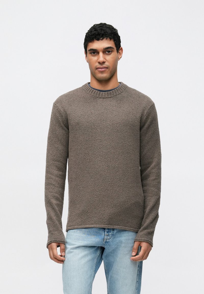 Ruskea teksturoitu neulepaita pyöreällä pääntiellä ja pitkillä hihoilla, yhdistetty vaaleansinisiin farkkuihin. Kangas näyttää pehmeältä ja miellyttävältä.