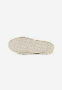 Suela de zapato de goma beige texturizada, con un patrón geométrico y acentos elevados. Bordes redondeados y material flexible visible.