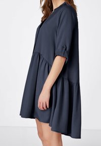 Vestido azul marino con mangas cortas, puños abotonados y falda acampanada. Hecho de tela ligera con una textura suave y diseño en capas.