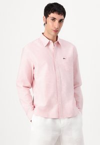Langermet skjorte med knapper i lys rosa med tynne hvite striper. Har en brystlomme og en grønn logo. Myk bomullsstoff.