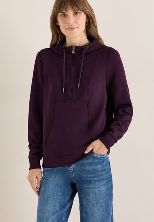 Sudadera con capucha morada, con bolsillo frontal, puños acanalados y cordones ajustables. Textura suave, corte casual. Combinada con pantalones vaqueros azules.