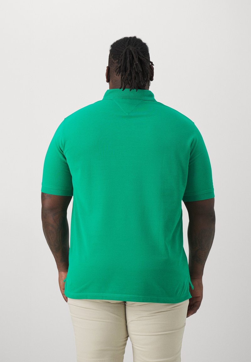 Polo-shirt vert à manches courtes en tissu doux. Il présente un col classique et un ourlet droit, porté avec un pantalon de couleur claire.