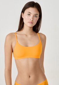 Orangene Bralette mit dünnen Trägern, glatter Textur und einem einfachen, minimalistischen Design. Keine Beschläge oder Muster sind sichtbar.