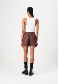 Shorts marron avec une taille élastique, associés à un débardeur blanc. La modèle porte des bottes noires à talons épais. Design simple et minimaliste.