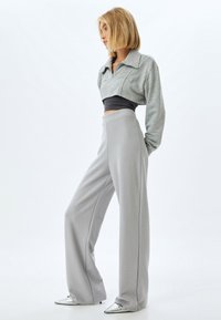 Jasnoszara, krótka bluza z kołnierzykiem, zestawiona z wysokim stanem szarymi spodniami w szerokiej nogawce oraz srebrnymi, spiczastymi butami. Gładka faktura, minimalistyczny design.