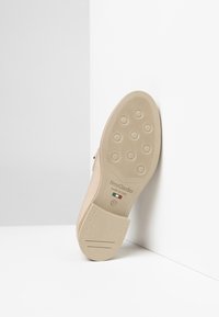 Beige lædersko med en struktureret gummisål, der har cirkulære greb, prægede brandlogo og et glat, elegant design. Størrelse 37.