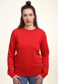 Felpa rossa in cotone con maniche lunghe e scollatura a girocollo. Texture morbida, vestibilità rilassata e polsini a coste. Abbinata a jeans in denim blu.
