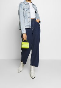 Denimjacka i ljusblått, croppad vit topp, mörkblå vida byxor, grön mini-handväska, vita ankelskor med snakeskin-mönster.