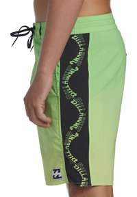 Shorts de bain verts avec panneau latéral noir affichant le texte « Billabong » en vert dans un motif en vagues. Équipés d'un cordon de serrage et d'un patch logo.