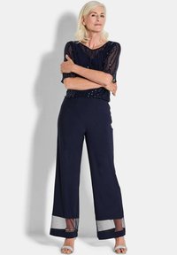 Marineblauwe outfit met een doorschijnende, met sequins bedekte top en wijde broek met een gaasaccent aan de zoom. Sandalen voegen een elegante touch toe.