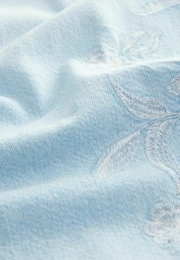 Heledsinine denim kangas, millel on valged lillemustrid, pehme tekstuur ja värvi kerge varieerumine, mis on loodud kanga kudumise teel.