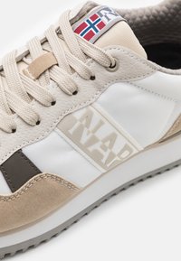 Sneaker beige e bianco caratterizzato da una combinazione di materiali in pelle e tessuto, con colletto imbottito, suola in gomma e un accento del logo.