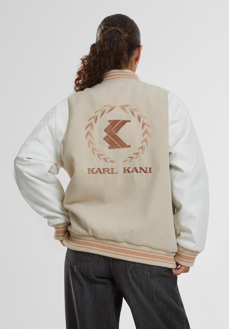 Bēžs bomberjaka ar baltām piedurknēm, ribotām aprocēm un apkakli. To raksturo izšūts logo un lauvas dizains uz aizmugures.