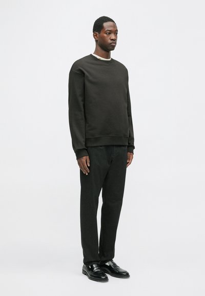 Ciemnobrązowy sweter o swobodnym kroju, okrągłym dekolcie i ściągaczach, w połączeniu z dopasowanymi czarnymi spodniami i eleganckimi czarnymi butami.