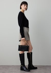 Fekete hosszú ujjú felső, szürke miniszoknya. Fekete térdig érő csizma arany díszítéssel. Kis fekete kézitáska láncos pánttal és arany szerelékkel.