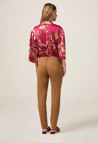 Satijnen shirt in magenta met bloemenpatroon, gecombineerd met lichtbruine op maat gemaakte broek. Gezicht van de achterkant, met een relaxte pasvorm en korte mouwen.
