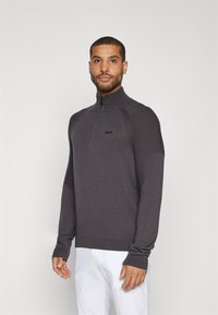 Halb-Zip-Pullover aus dunkelgrauem Strick mit gerippten Bündchen und Schulterakzenten. Besitzt ein dezentes Logo auf der Brust und eine glatte Textur.
