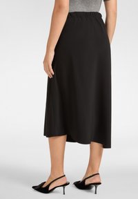 Schwarzer Midirock mit elastischem Taillenbund, glatter Textur und leichtem A-Linien-Schnitt. Kombiniert mit schwarzen Slingback-Heels mit einer Schleifendetail.