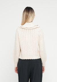 Lys rosa ribbet genser med volangkrage og ballongsleeves, laget av et mykt, teksturert stoff, som ender ved midjen.