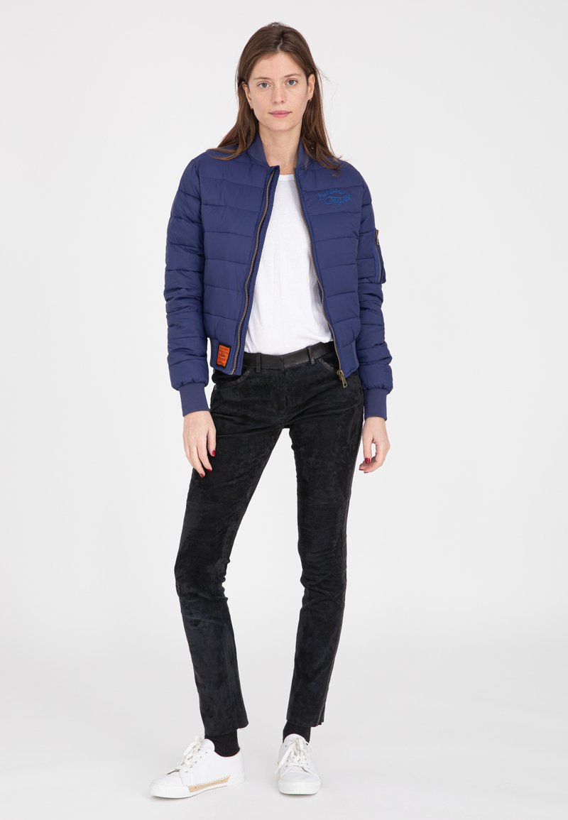 Giacca puffer blu navy con zip frontale e polsini a costine, abbinata a pantaloni neri in tessuto testurizzato e sneakers bianche. Design semplice e casual.