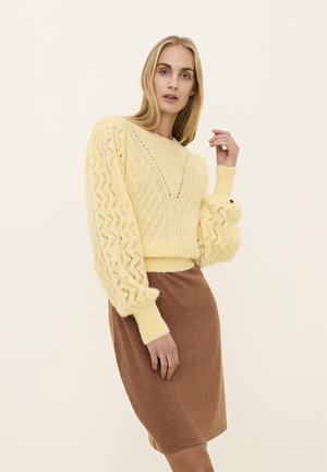 Yellow knitted sweater with a textured, patterned body and puffed sleeves, paired with a brown ribbed skirt, both in a neutral setting.