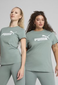 Pár krátkých rukávů, světle zelených bavlněných triček s bílým logem "PUMA", nošených s odpovídajícími světle zelenými legínami.