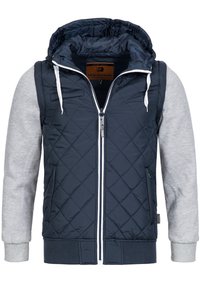 Chaqueta acolchada navy con mangas grises, capucha, cremallera blanca y cordones; presenta puños y dobladillo acanalados para mayor textura.