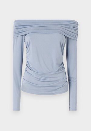 Svetlo modra bluza z odkrito ramo, izdelana iz gladkega materiala, ki ima guban detajl okoli izreza in pasu ter dolge rokave.