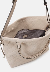 Sac à main matelassé beige avec une surface texturée, doté d'une poche intérieure zippée et d'une longue sangle réglable.