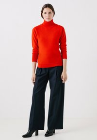 Maglione rosso a collo alto con maniche lunghe, abbinato a pantaloni ampi blu navy con righe verticali, completato da stivali neri con tacco.