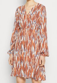 Vestido multicolorido con escote en V, mangas largas y cintura elástica. Presenta un patrón de franjas en óxido, azul y crema en una tela ligera.