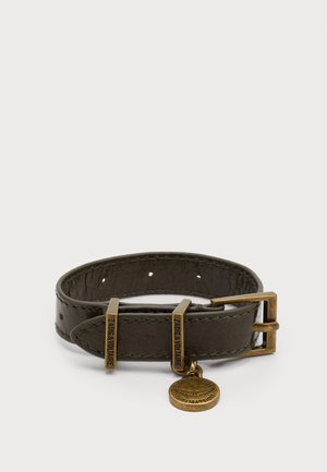 Bracelet en cuir marron avec boucle en métal, présentant deux accents métalliques gravés et un charm circulaire suspendu. Surface texturée et trous ajustables.