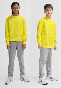 Två barn har matchande klara gula långärmade tröjor, i kombination med grå sweatpants och vita sportskor.