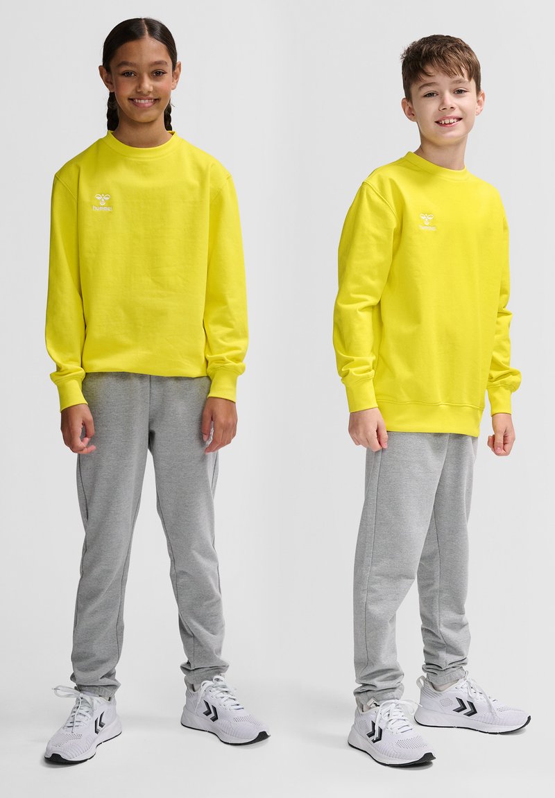 Två barn har matchande klara gula långärmade tröjor, i kombination med grå sweatpants och vita sportskor.