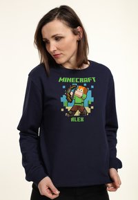Felpa blu navy in cotone, con un personaggio pixelato di Minecraft di nome Alex, che tiene un arco, con accenti verde e marrone.