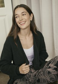 Cardigan negru, texturat, cu o croială lejeră, purtat peste un top alb. Pantalonii cu model au un design ondulat în nuanțe de roz și negru.