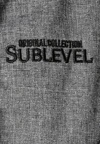 Texture de tissu avec texte brodé noir indiquant "MODERN COLLECTION SUBLEVEL" sur un fond gris tissé.