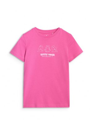 Dziewczyna stoi, ubrana w fioletową bluzę z suwakiem i spodnie oraz jasnoróżowy t-shirt z ilustracjami kotów uprawiających jogę.