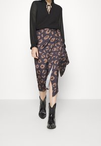 Donna che indossa una blusa nera a maniche lunghe, una gonna avvolgente a stampa leopardata marrone e nera con spacco frontale e stivaletti cowboy neri alla caviglia, mentre cammina in avanti.
