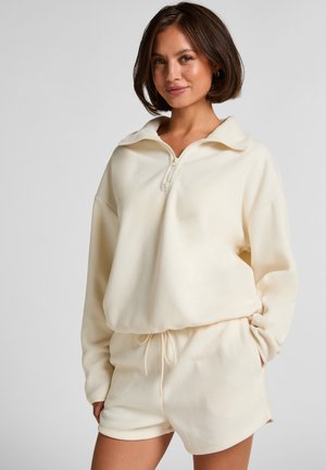 Cremefarbenes Sweatshirt- und Shorts-Set aus weichem Stoff. Das Sweatshirt verfügt über einen halben Reißverschluss und eine lockere Passform; die Shorts haben einen elastischen Bund.