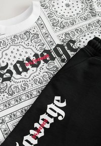 Hvid bandana-mønstret skjorte med sort gotisk tekst og rødt broderet ord "street," kombineret med sorte bukser med lignende hvid og rød tekst.