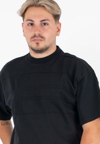 Zwarte t-shirt met korte mouwen en een hoge hals, met een patroon van textuurlijnen in horizontale richting op de voorkant. Gladde katoenen stof, rechte pasvorm.
