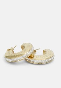Guld hoops øreringe med en række klare krystaller, graveret med "LOVE GUESS," med en glat metallisk finish og et buet design.