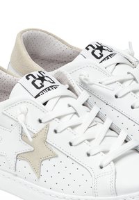Sneaker bianche in pelle liscia con dettagli perforati. Presentano un accento a forma di stella beige, lacci bianchi piatti e un'etichetta con il marchio sulla linguetta.